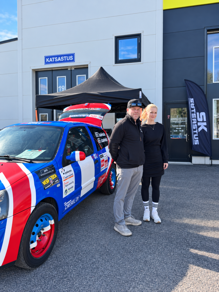 Ralliauto ja kaksi henkilöä SK Katsastuksen pihalla.